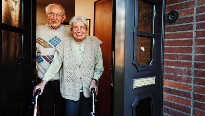 twee oude mensen, één met rollator, bij de voordeur